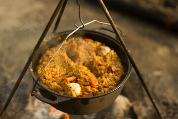 Cooking camping outdoor meal in an open fire in a travel pot with blaze. Dinner during travel.