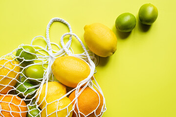 ripe whole citrus fruits in string bag on yellow background