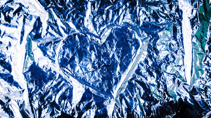 Abstract background. Heart shape in the middle of a crumpled aluminum foil.