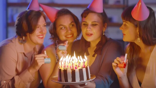 Woman blowing out candle on cake at birthday party with friends at home