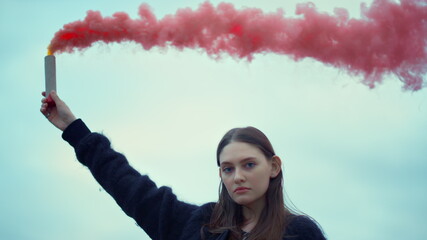 Girl holding smoke bomb in hand at street protest. Woman using smoke grenade