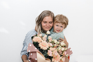 son and young mother hug and kiss. the child congratulated his mother on her birthday and presented bouquet 