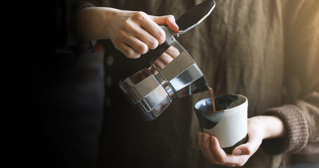 Barista pouring coffee from moka pot coffee maker to the small coffee cup . Professional coffee brewing.