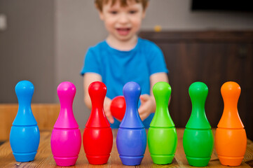 Children a boy throws ball into a home bowling alley and smashes the bowling pins. Selective focus. concept of active play in the home room, quarantine, self-isolation, achieving goal.