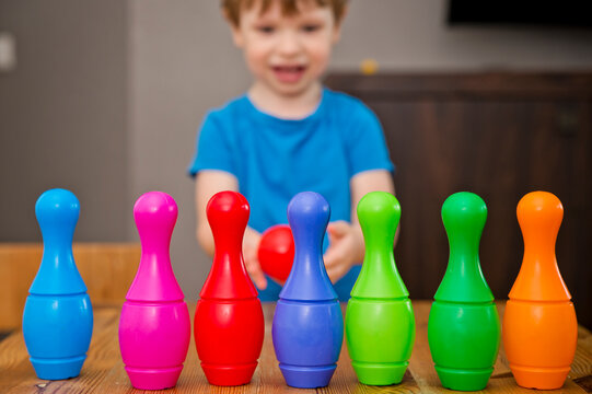 Children A Boy Throws Ball Into A Home Bowling Alley And Smashes The Bowling Pins. Selective Focus. Concept Of Active Play In The Home Room, Quarantine, Self-isolation, Achieving Goal.