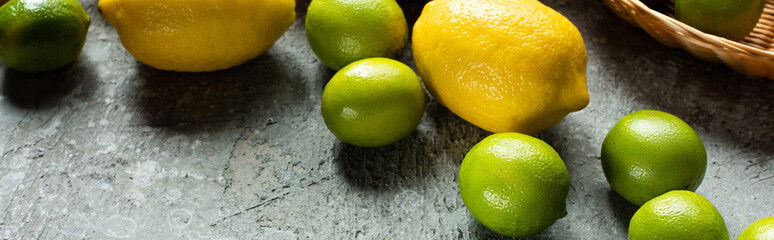 ripe yellow lemons and green limes on concrete textured surface, panoramic crop