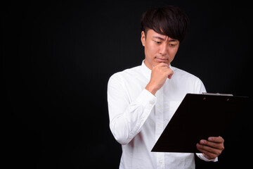 Young handsome Asian businessman against black background