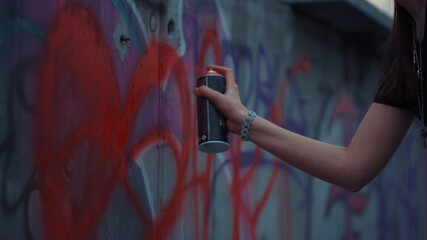 Woman hand painting graffiti on street wall. Girl drawing red heart on building