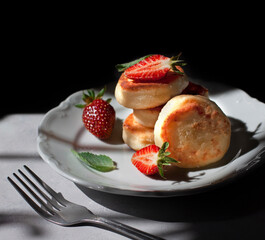 Cheesecakes or cottage cheese pancakes with fresh strawberries on a white plate. Russian sweet Breakfast syrniki. Dark background