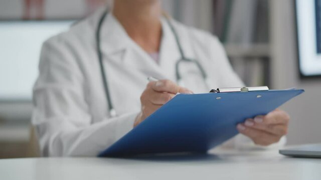 Close up of doctor filling patient history list in clipboard sitting in hospital office.