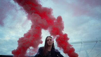 Girl posing at camera in colorful smoke. Attractive woman holding smoke bombs