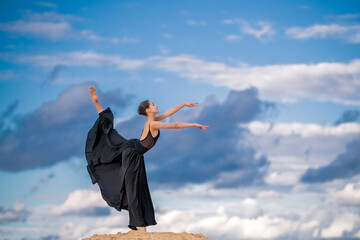 young ballerina in a black long dress hovers above the ground like a bird, resisting a gust of wind...