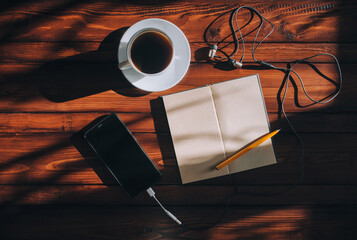 Paper notebook and black smartphone with empty screen, pen, headphone and cup of coffee lies on a brown wooden background mahogany. Copy space and mockup. Music and writter concept.