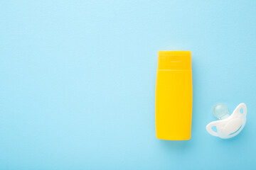 Yellow plastic tube of sunscreen and white soother on light blue table background. Pastel color. Care about body skin protection in hot summer. Closeup. Empty place for text or logo. Top down view.