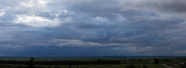 Storm clouds cover the landscape. Tragic gloomy sky. Panorama. Village in the steppe. Fantastic skies on the planet earth.