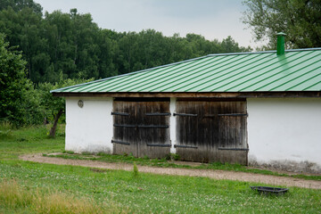 Fototapeta na wymiar stone white old animal shed with metal green roof on forest background