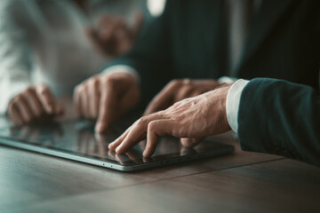 Business People touching screen of digital tablet while working together. Close up of human hands. Selective focus on male hands in foreground. Teamwork concept. Tinted image.