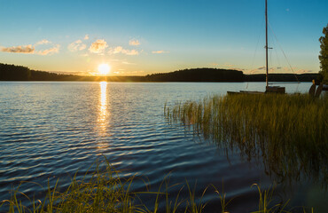 Sunset on a forest lake on a summer evening. The sun sets behind a distant forest