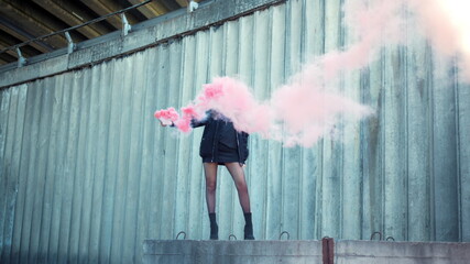 Girl standing on street with smoke bomb in hand. Woman holding smoke grenade