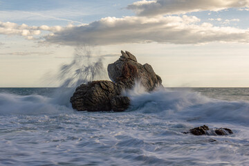 roca en medio del mar parecida a un barco y con una mar brava y nubes en el cielo