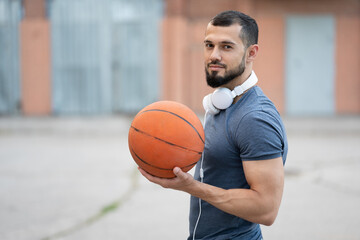 Fototapeta premium Man with headphones stands on the street with a basketball in his hands
