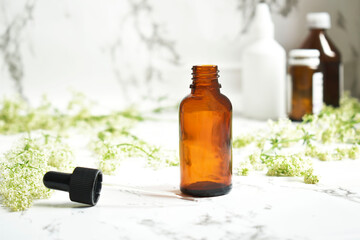 Essential oil in an amber glass bottle, with a glass dropper and thyme flowers on a marble table.