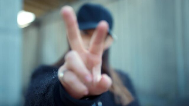 Girl showing v sign at camera on street. Woman showing peace sign with fingers