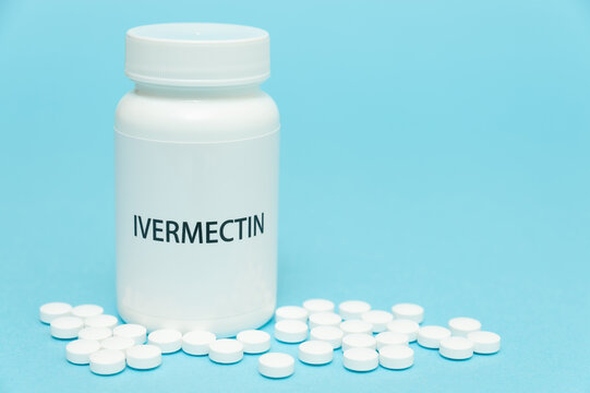 Treatments for Coronavirus (COVID-19): IVERMECTIN in white bottle packaging with scattered pills. Isolated on blue background. Horizontal shot. Copy space.