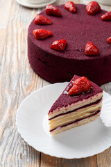 A slice of purple red velvet torte with fresh strawberries on old wooden table