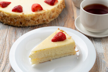 Classic cheesecake with strawberry on a top, served with cup of tea on rustic wooden table