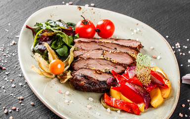 Grilled veal steak with salad and vegetables in plate on dark stone background. Hot Meat Dishes, top view