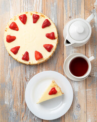 Directly above advertisement photo of classic american cheesecake on wooden table with a cup of tea and teapot