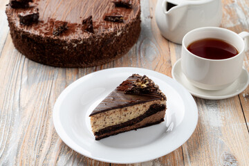 A slice of classic chocolate birthday torte on a wooden table with a cup of black tea