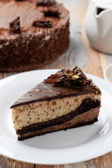 A slice of classic chocolate birthday torte on a wooden table with a cup of black tea