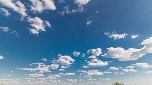 White clouds mooving on a blue sky over green field with grass and trees timelapse