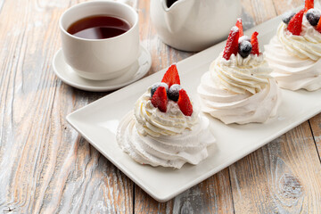 Three small portions of anna pavlova meringue dessert, topped with blueberry and strawberry on wooden table, close up