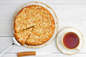Homemade gooseberry pie garnished with almond petals and cup of tea on white wooden table. Top view.