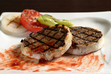 Two roasted beef cutlets from steak on plate close-up with grilled vegetables of tomato, onion and bell pepper. Photos for restaurant and cafe menus