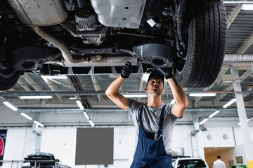 low angle view of technician in cap and overalls repairing car in service station