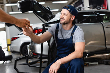 mechanic giving paper cup to cheerful coworker in cap