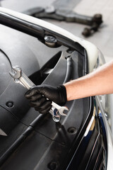 Cropped view of auto mechanic in latex glove holding wrenches near open hood