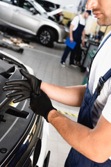 Fototapeta na wymiar cropped view of mechanic in uniform wearing latex gloves near car in workshop