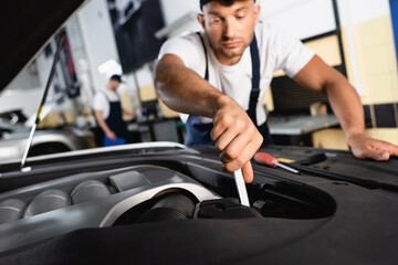 Fototapeta na wymiar selective focus of handsome mechanic in cap repairing car near coworker in workshop
