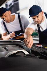 Fototapeta na wymiar selective focus of mechanic in uniform repairing car near coworker with clipboard and pen
