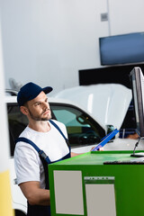 handsome mechanic in cap looking at computer monitor in workshop