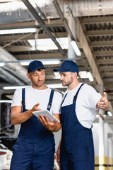 handsome mechanics in uniform using digital tablet and gesturing in workshop