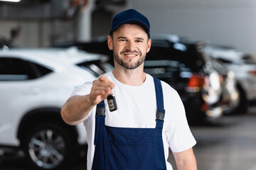 cheerful mechanic in uniform and cap holding car key