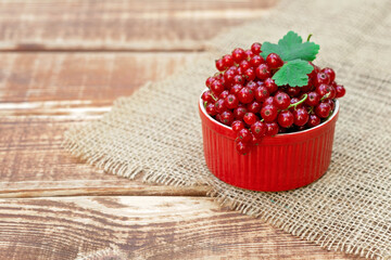 Red currant berries in a cocotte bowl on a wooden background with burlap. Natural vitamins concept.