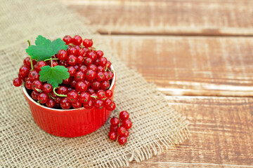 Red currant berries in a cocotte bowl on a wooden background with burlap. Natural vitamins concept.