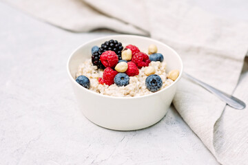 Oatmeal with raspberries, blueberries, blackberries and nuts on a gray concrete background. Healthy healthy breakfast.